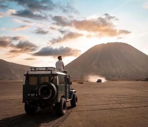 Hamparan luas pasir berbisik Bromo dengan pegunungan kaldera Tengger di latar belakang.